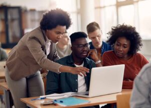 Teacher working with students in a classroom with a laptop