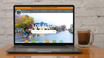 Coffee and Laptop on a wooden table. Laptop screen shows the website homepage of Los Altos