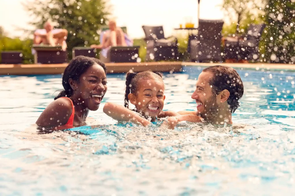 A family of 3 in a swimming pool splashing water.
